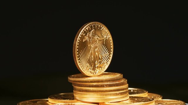 A single US Mint Gold Eagle coin stands vertically on a stack of golden coins and rotates showing the Liberty side of the bullion