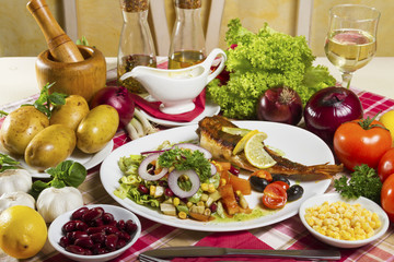 Fried scorpaena scrofa with salad on the plate and serving at the table with fresh vegetables, sauce, glass of white wine and olive oil.