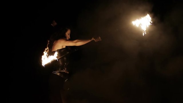 Female fire dance performer dancing with burning fire on black background. Brunette woman juggles with fireballs dance show outdoors