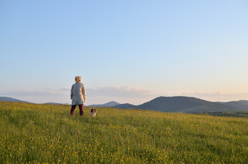 Woman with her dog in a mountain meadow watching landscape