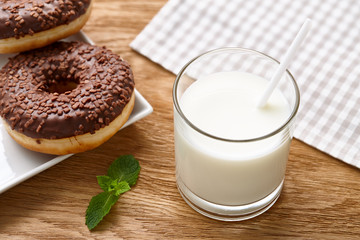 Glass of milk and chocolate donuts on wooden table