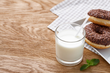 Glass of milk and chocolate donuts on wooden table