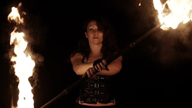 Close-up portrait of female fire dance performer dancing with burning fire on black background. Brunette woman juggles with fireballs dance show outdoors