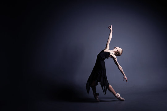 Young ballerina in a black suit is dancing in a dark studio