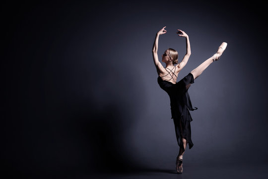 Fototapeta Young ballerina in a black suit is dancing in a dark studio