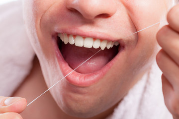 Young man cleaning her white teeth with dental floss