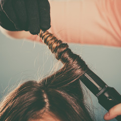 Hairdresser curling woman hair with iron curler.