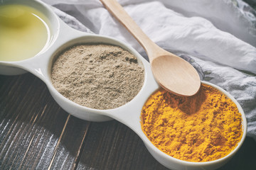 Turmeric, black pepper and olive oil in white ceramic bowl on wooden background. Ingredients for golden paste