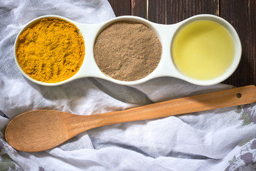 Turmeric, black pepper and olive oil in white ceramic bowl on wooden background. Ingredients for golden paste