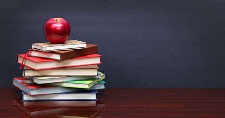 Pile of books and red apple on the desk over the blackboard - 118025821