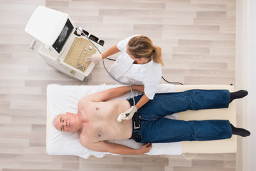 Doctor Using Ultrasound Scan On Abdomen Of Senior Male Patient