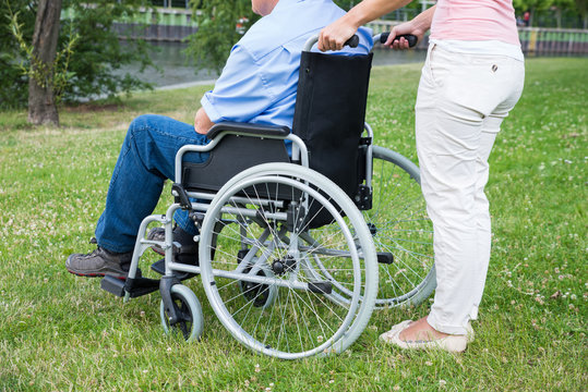 Woman Assisting Disabled Man On Wheelchair