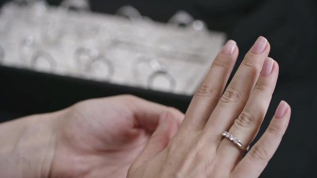 Closeup of female hand putting silver wedding ring with diamonds on her finger in jewelry store