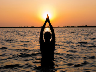 A man in meditation and prayer as he stand in a holy river at dusk.