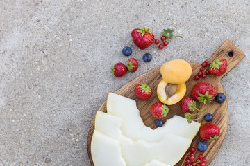 Top view on wooden board with fresh organic fruit and berries: melon, strawberries, blueberries, apricot and red current on concrete background. Healthy snack