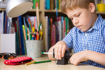 Portrait of cute school boy sitting at his desk and sharpening pencils. Child preparing for lessons.