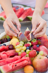 Womans hands putting summer organic fruit on the plate: Melon, peach, strawberries, blueberries, apples, figs, cherries, apricots, watermelon and grapes. dessert or snack. Healthy food concept.