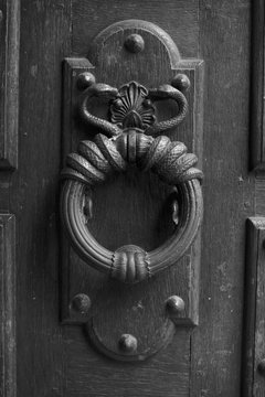Royal style doorknocker on old wooden door. Paris, France. Aged photo. Black and white.