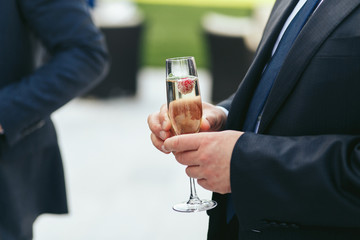 Man in black suit holds  a glass with champagne and strawberry