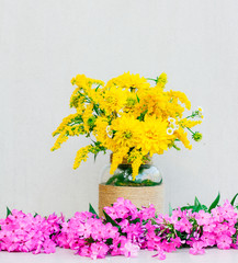 a bouquet of flowers chrysanthemums, goldenrod and daisies in a vase among the Phlox on a gray background. tinted photo