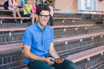 Portrait of teacher sitting on bench and using digital tablet