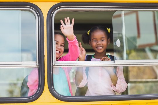 Portrait of school kids waving hand from bus 