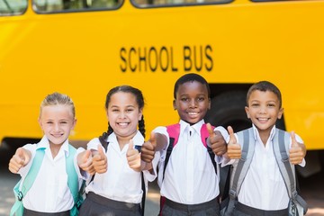 Smiling kids showing thumbs up in front of school bus