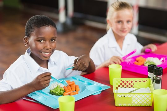 Boy and girl in school uniforms having lunch in school cafeteria