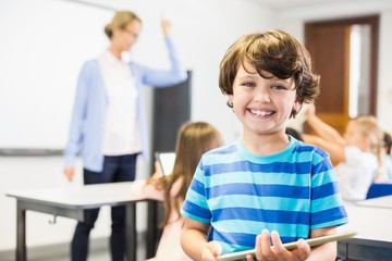 Portrait of schoolboy holding digital tablet in classroom
