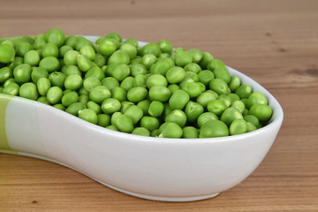 Green peas in a ceramic bowl, wood background