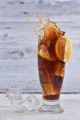 Lemon slice splashes in a full of cola and ice cubes glass
