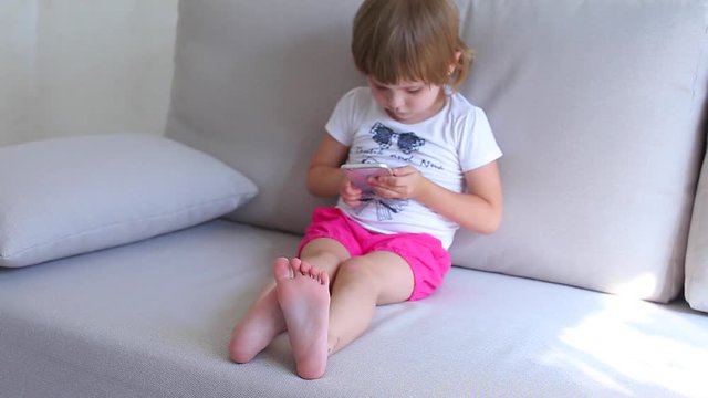 Little girl plays on phone and smille looks to camera