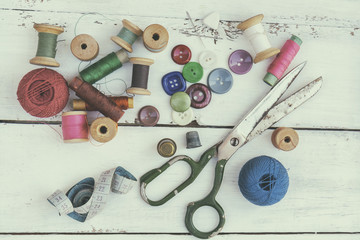 Set of several pied buttons for garment with threads, garment tape and scissors on a bright wooden background. Toned and processing photos with soft focus in vintage style.