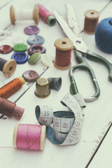 Set of several pied buttons for garment with threads, garment tape and scissors on a bright wooden background. Toned and processing photos with soft focus in vintage style.