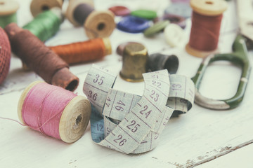 Set of several pied buttons for garment with threads, garment tape and scissors on a bright wooden background. Toned and processing photos with soft focus in vintage style.