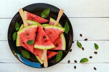 Pieces of ripe watermelon on a stick on a black plate on a white background. The top view.
