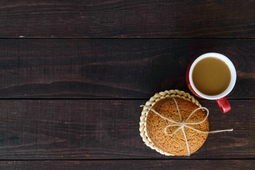 A cup of cappuccino and oatmeal cookies, tied with twine on dark wooden background. top view