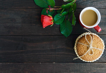 A cup of cappuccino, rose and oatmeal cookies, tied with twine on dark wooden background. top view