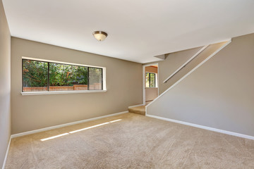 Empty beige room with staircase and carpet floor.