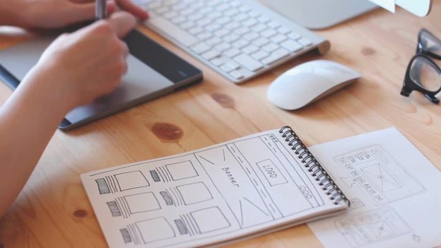 A web designer works on the graphics tablet, the site layout drawn with sketch book.