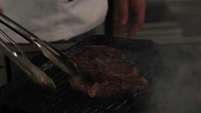Chef preparing rib eye steak on grill, close up
