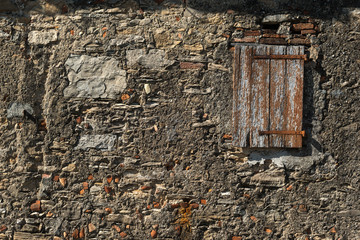 Vecchio muro in pietra con finestra chiusa da anta di legno con cardini arrugginiti