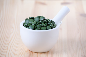 green spirulina chlorella seaweed pills in a white bowl on the wooden