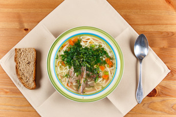 Chicken soup in ceramic bowl with piece of bread and spoon