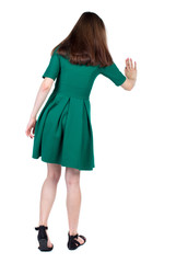 back view of woman. Young woman presses down on something. Isolated over white background. Rear view people collection. backside view of person. The slender brunette in a green short dress presses a