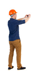 Backview of an engineer in construction helmet stands and using photo camera. Standing young guy. Rear view people collection.  backside view of person.  Isolated over white background.  a man in a