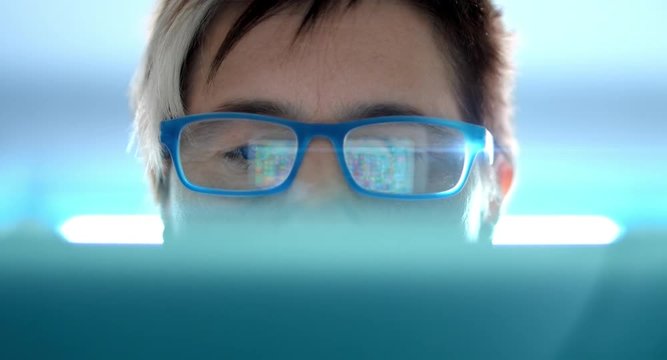 4K: Eine Frau benutzt ein Tablet f&uuml;r ein online Spiel, das sich in ihrer Brille widerspiegelt. Ihr Gesicht ist halb bedeckt. Der Hintergrund zeigt eine bl&auml;uliche technologische Umgebung mit Lensflare