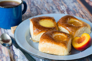 Freshly baked buns.   Freshly baked buns with apricot jam on an old metallic a plate and a mug of of tea on a wooden table.