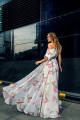 Full growth portrait of fashionable woman in fluttering long dress on urban background