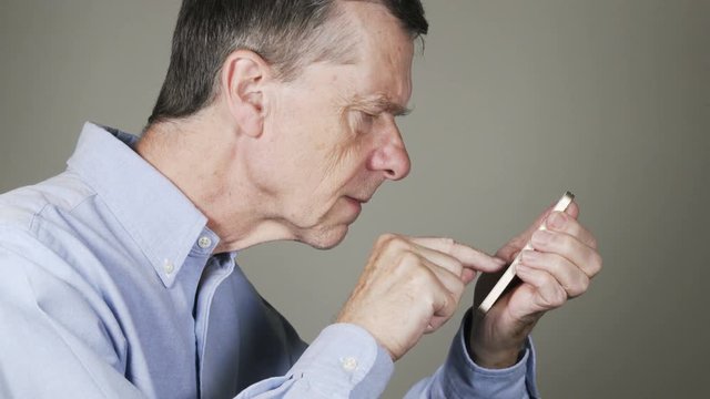 Close shot of a senior caucasian man struggling to read the screen on small smartphone to send a message or access an App showing problems with modern technology